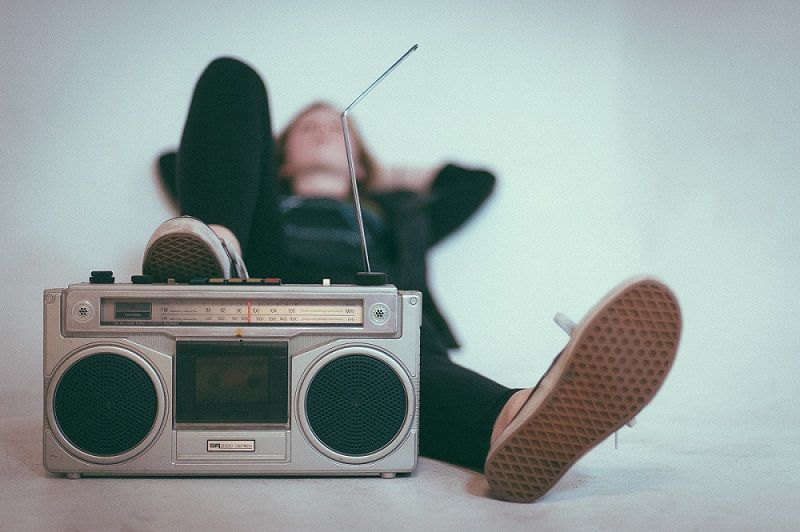 A blurry shot of a woman in sneakers reclining with her foot on a vintage sound system.